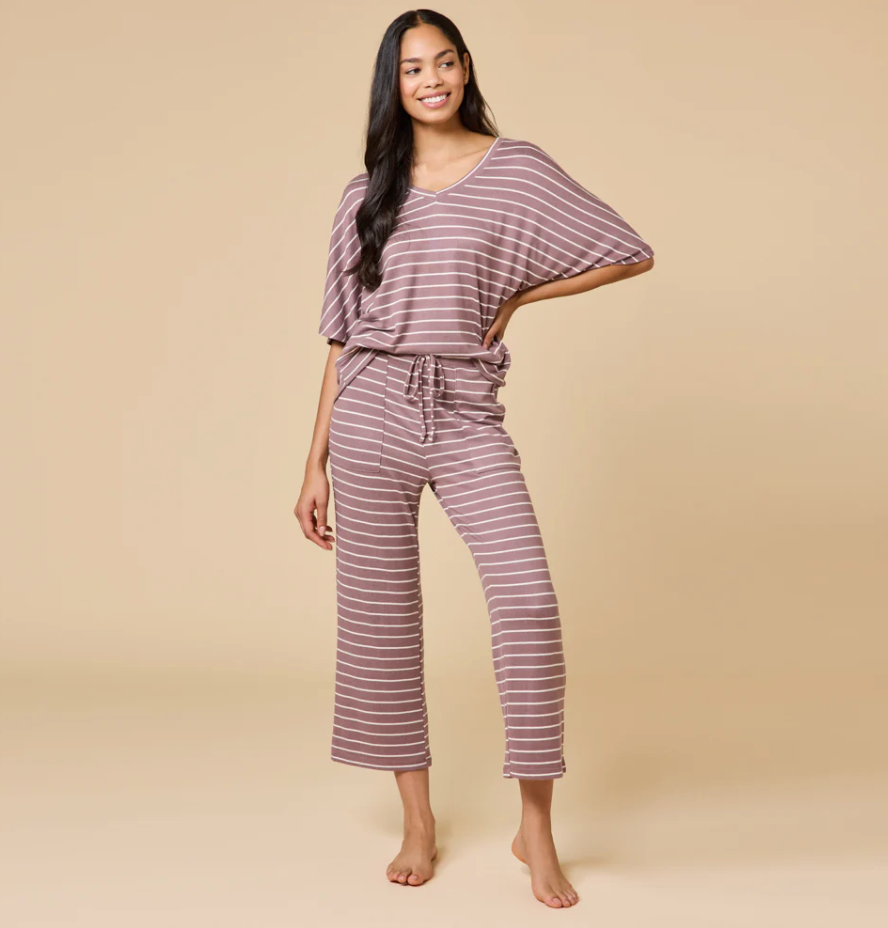 Studio photograph of a woman modeling a mauve and white horizontal striped loungewear set featuring a v-neck top and drawstring wide-leg pants against a neutral tan backdrop