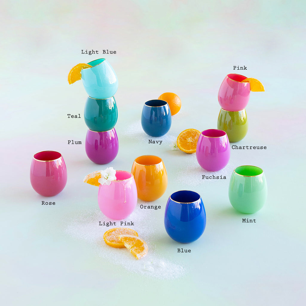 Collection of colorful stemless glasses with gold rims labeled by color with orange slices and sugar