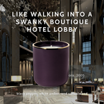 Dark purple candle with gold rim against a luxury hotel lobby background