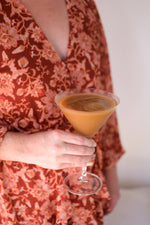 Person holding a martini glass filled with a tan colored cocktail