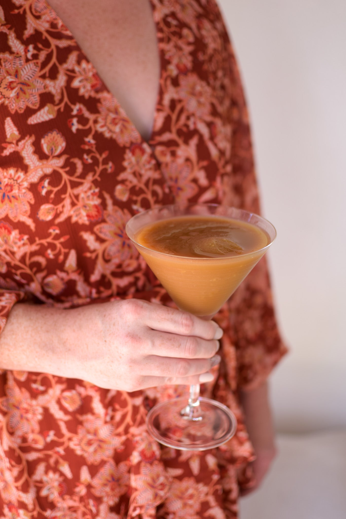 Person holding a martini glass filled with a tan colored cocktail