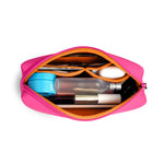 An open hot pink cosmetic bag with an orange interior filled with a blue jar, a frosted bottle, and a L'Oreal beauty product neatly organized by orange elastic bands