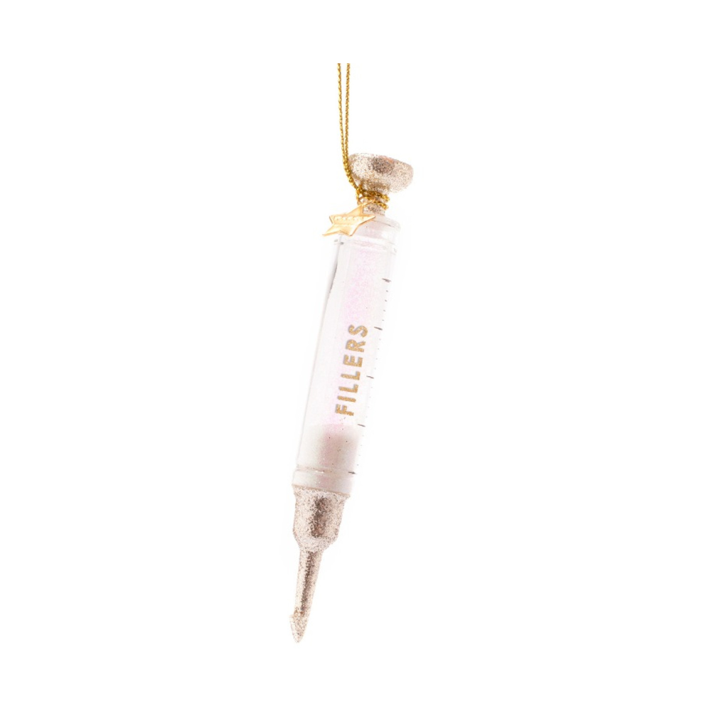 Glass decorative syringe ornament filled with pink glitter, featuring "FILLERS" in gold lettering, a sparkling gold plunger and needle tip, and hanging from a gold string with a small gold star