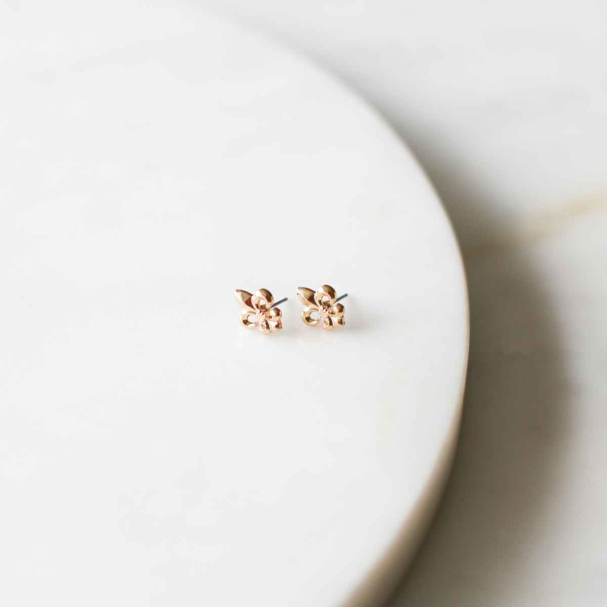 Two small rose gold floral stud earrings with tiny clear stones centered on a clean white marble surface