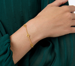 Gold chain bracelet with three clover charms worn on a wrist against a green fabric background