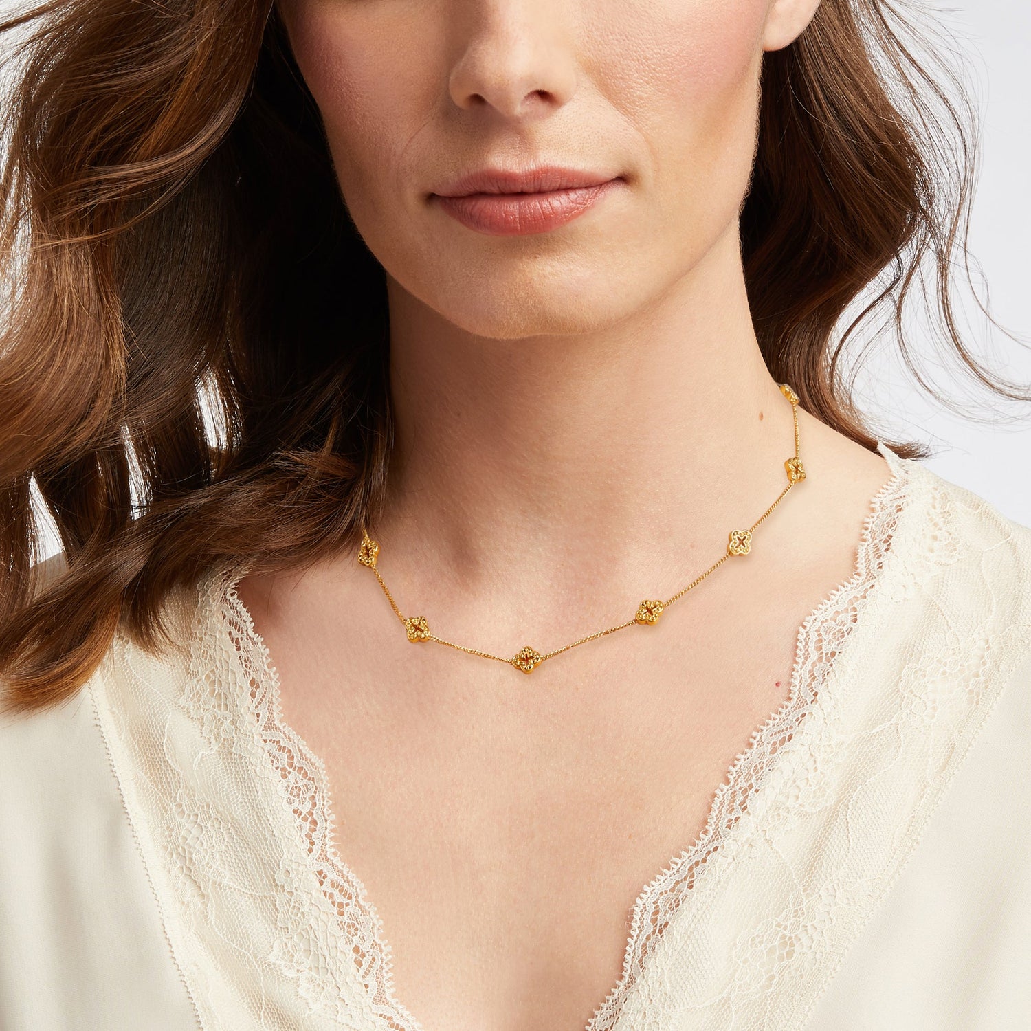 Woman wearing a gold chain necklace with small clover shaped charms