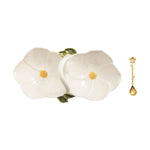 Ceramic two-part flower-shaped serving dish with yellow centers and green leaves accompanied by a gold branch-design spoon with a flower handle