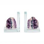 A pair of contemporary glass bookends each holding a rough cut banded fluorite crystal in vibrant purple green and white hues