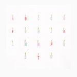 Photograph of gold-toned enamel alphabet letter charms in pastel pink, light blue, and purple, featuring uppercase letters A through W, arranged neatly in rows on a clean white background