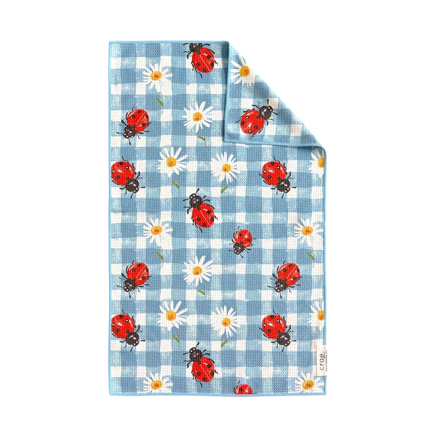crae. patterned textile featuring red ladybugs with black spots and white daisies with yellow centers on a blue and white gingham background with a subtly folded top right corner