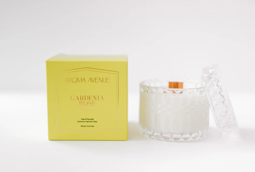 Yellow Aroma Avenue Gardenia Rose candle box next to a faceted glass candle jar with lid
