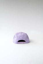 Photograph of a lavender purple baseball cap on a white background shown from the rear, highlighting its plastic snap closure and stitched panels