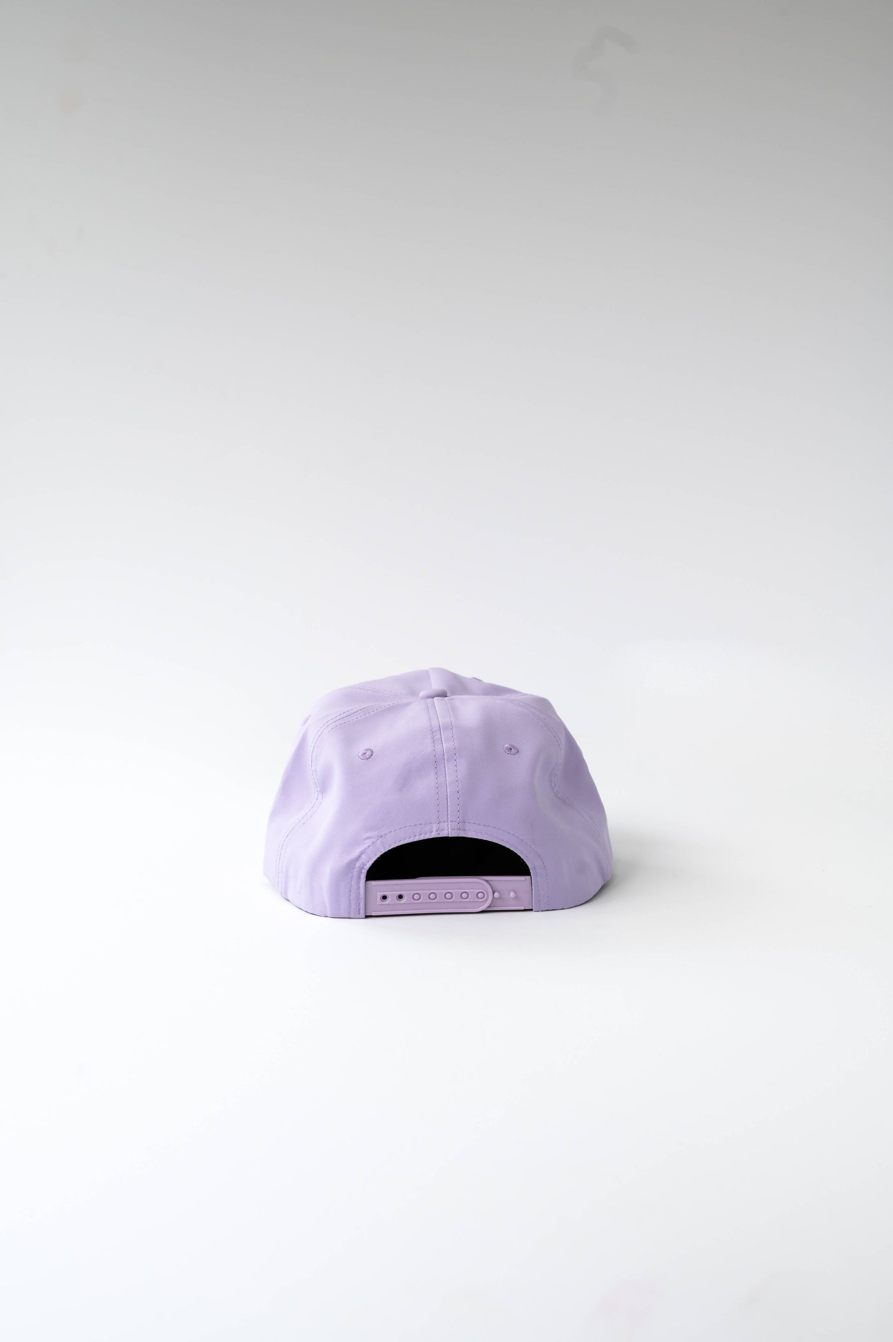 Photograph of a lavender purple baseball cap on a white background shown from the rear, highlighting its plastic snap closure and stitched panels