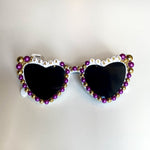 White heart-shaped sunglasses featuring black lenses adorned with purple and gold beads and the words GEAUX on the left frame and TIGERS on the right frame