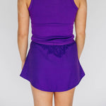 Person wearing a purple tank top and matching athletic skirt from the back