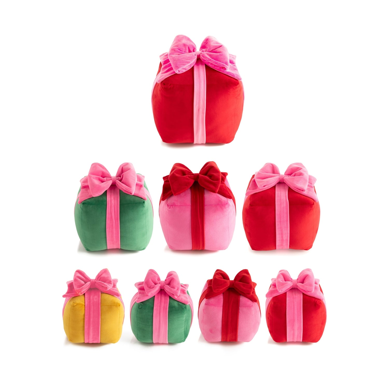 Studio shot of seven soft velvet gift box pillows in red, green, pink, and yellow, each tied with contrasting pink or red bows against a white background