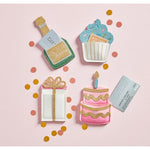 Four festive felt gift card holders shaped like a green champagne bottle, a blue glitter cupcake, a white gift box with a gold bow, and a pink two-tier cake with a candle, each holding a gift card, are arranged on a light pink surface with scattered gold and coral confetti