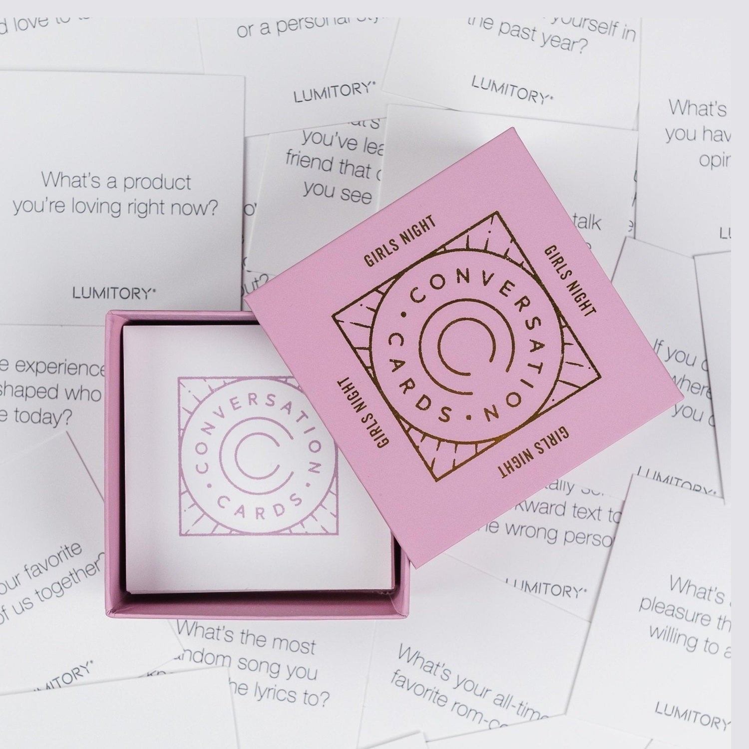 Pink Lumitory conversation cards box open on a surface covered with scattered question cards