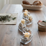 S-shaped glass candle holder with lit candles and decorative stones on a wooden table