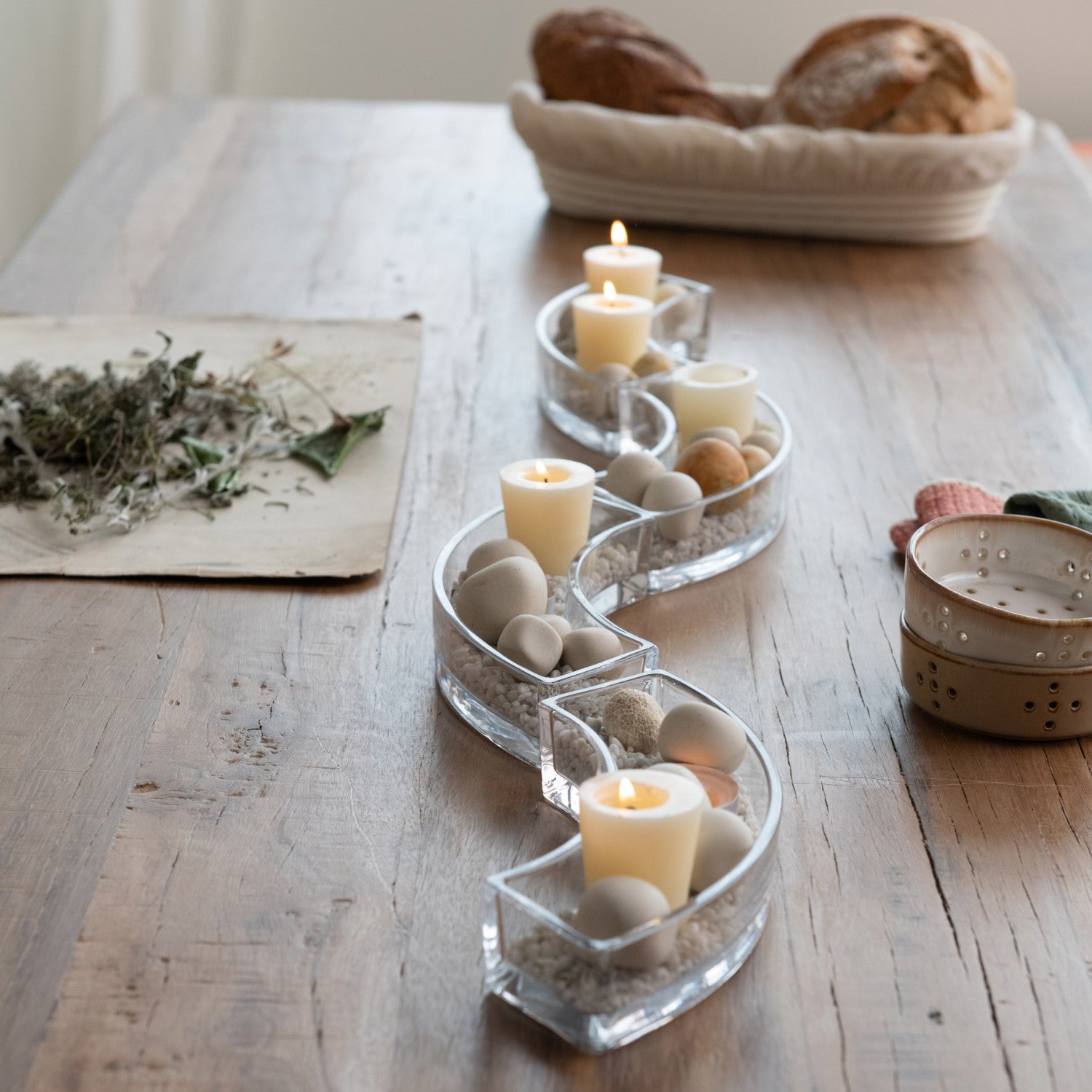 S-shaped glass candle holder with lit candles and decorative stones on a wooden table