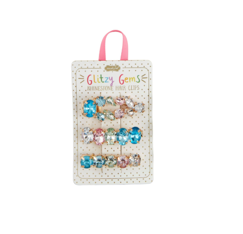 Product photography of a set of Glitzy Gems rhinestone hair clips on a polka-dotted card, featuring three rows of iridescent blue pink and clear oval stones in gold-tone settings with a pink ribbon hanger