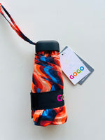 A GOGO mini umbrella displayed on a white background, featuring a vibrant wavy pattern in blues, reds, and oranges, with a black strap showing the colorful GOGO logo and a hang tag mentioning earth friendly and water repellent features