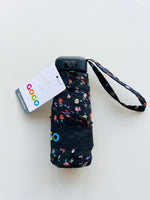 Product photo of a black GOGO Mini Umbrella with a vibrant multicolored floral pattern featuring pink orange blue and white flowers, an attached GOGO brand tag, and visible handle instructions for closing on a plain white background