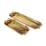 A pair of elongated gold-toned textured metal trays featuring decorative bow-shaped ends