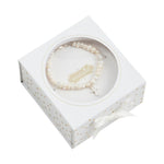 Mud Pie pearl bracelet featuring irregular white pearls and a silver cross charm presented in a white gift box with shimmering gold polka dots and a delicate white satin ribbon bow