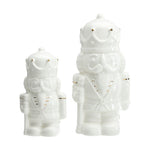 White ceramic figurines of two nutcracker soldiers in different sizes with subtle gold accents on their crowns and uniforms