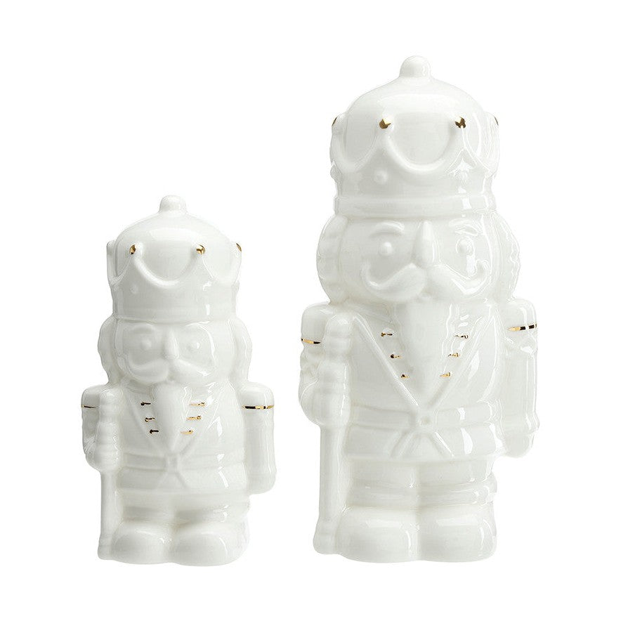 White ceramic figurines of two nutcracker soldiers in different sizes with subtle gold accents on their crowns and uniforms