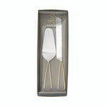 Product photograph by Santa Barbara Design Studio featuring a silver cake server and knife set with gold open-loop handles packaged in a clear gift box