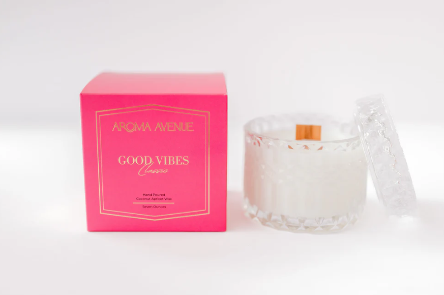 Aroma Avenue Good Vibes candle in a pink box next to a crystal glass candle jar with a lid