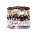 Product photography showing a vertical stack of eight elastic hair ties on a white background, featuring braided textures shimmering threads and oval beads in brown beige black navy pink and grey with the KINGSBURY brand name visible on a pink bead