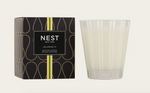 NEST New York Grapefruit Scented Candle shown with its dark box featuring a gold teardrop pattern and vertical lime green stripes, placed next to a clear glass vessel with subtle white vertical stripes