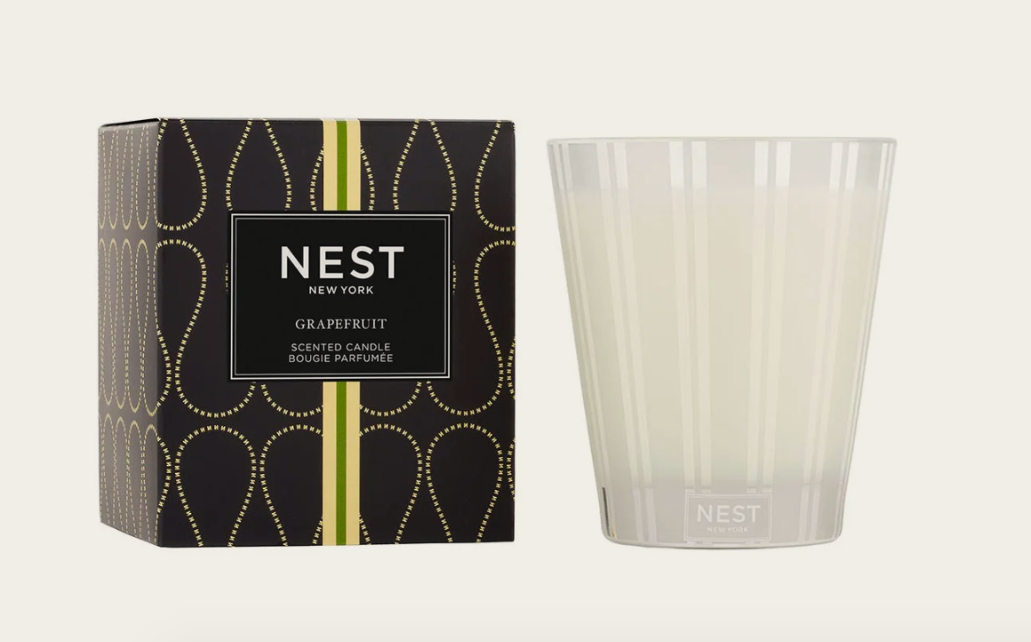 NEST New York Grapefruit Scented Candle shown with its dark box featuring a gold teardrop pattern and vertical lime green stripes, placed next to a clear glass vessel with subtle white vertical stripes