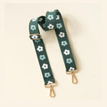 Dark green woven bag strap featuring an alternating pattern of white and light green embroidered flowers with gold-toned adjustable hardware and swivel clasp hooks
