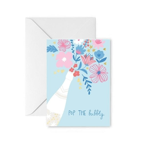 Digital illustration by Rifle Paper Co. of a white champagne bottle erupting with a vibrant pink and blue floral bouquet and the hand-lettered text POP THE bubbly on a light blue background