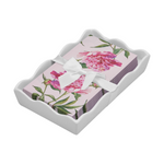 Decorative pink paper napkins featuring watercolor peony flowers and green foliage, tied with a white satin ribbon, presented in a wavy white ceramic napkin holder
