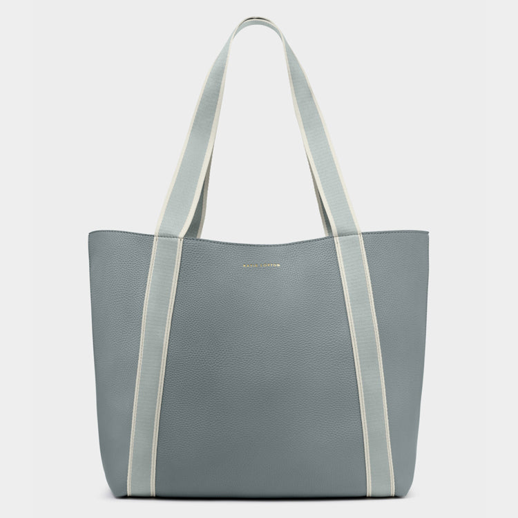 Katie Loxton product photo of a blue-grey pebbled faux leather tote bag on a plain background featuring two-toned light blue and cream webbing straps and subtle gold brand lettering
