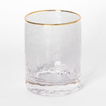 Clear cylindrical drinking glass with a distinctive hammered texture and a metallic gold rim on a plain white background