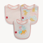 Fabric baby bibs, a set of three featuring diverse designs including pink and white stripes, a pastel floral pattern with yellow and blue accents, and a white bib with a vibrant bouquet of pink, blue, and yellow flowers alongside Magnolia Me text, all edged in pink with red brand tags