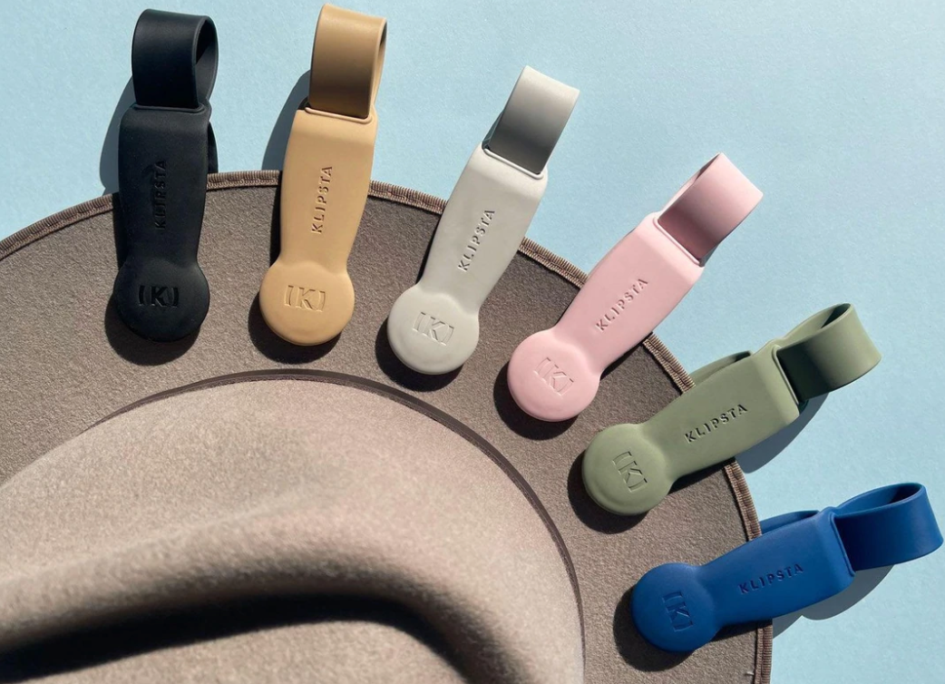 Six colorful Klipsta hat clips arranged in a fan shape on a beige felt hat