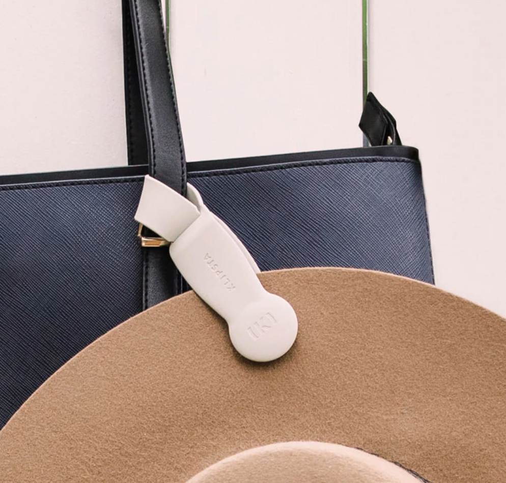 Beige hat clip attached to a black handbag strap holding a tan felt hat