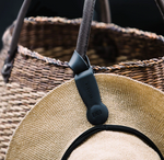 Black Klipsta hat clip attached to a woven bag handle holding a straw hat