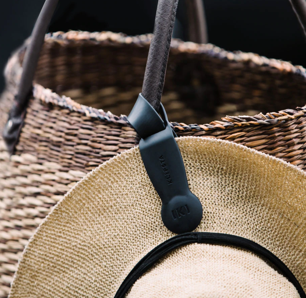 Black Klipsta hat clip attached to a woven bag handle holding a straw hat