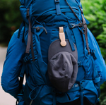 Grey baseball cap clipped to a blue hiking backpack with a tan accessory clip