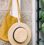 Straw hat attached to a mustard yellow canvas tote bag hanging on a wall