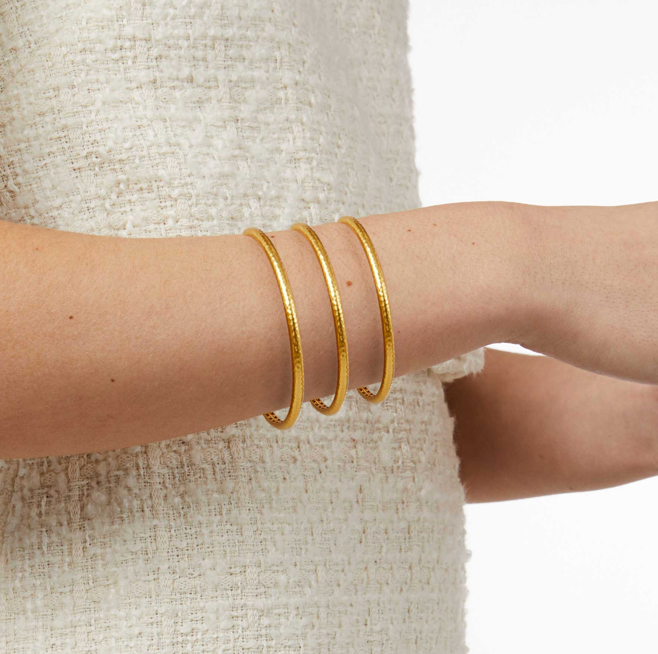 Three thin gold hammered bangles worn on a wrist