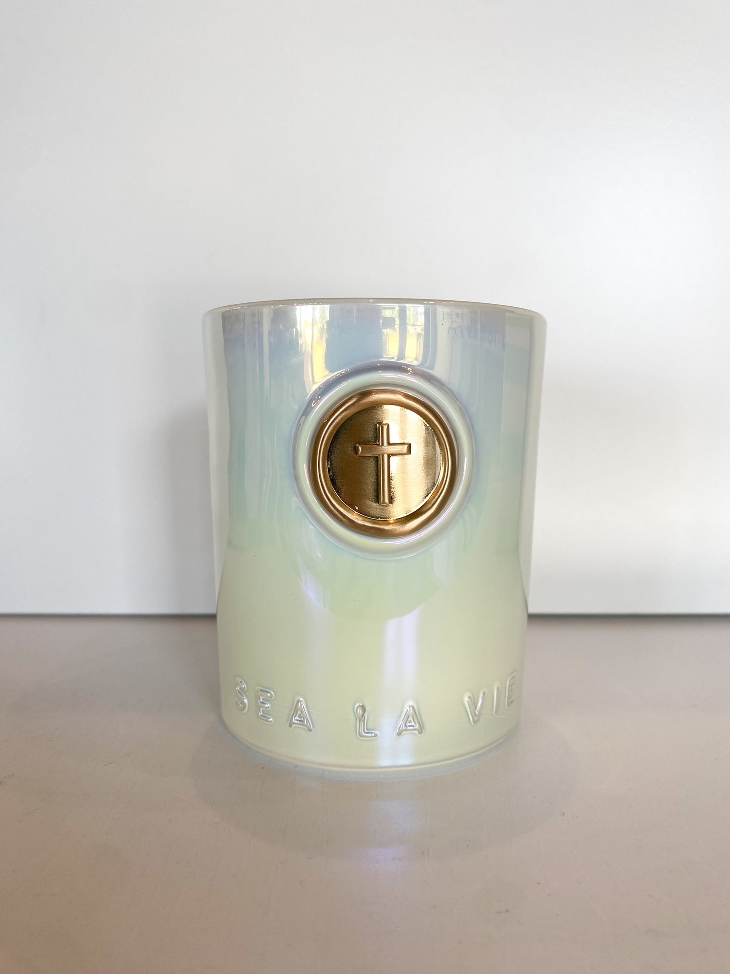 Iridescent candle jar with a gold cross emblem and embossed text